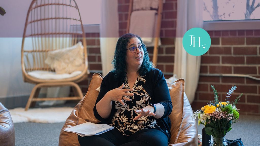 Jossie Hianes, leadership coach for women in tech, is sitting on a chair, talking with a group of women about leadership. She is gesturing with her hands as she speaks.