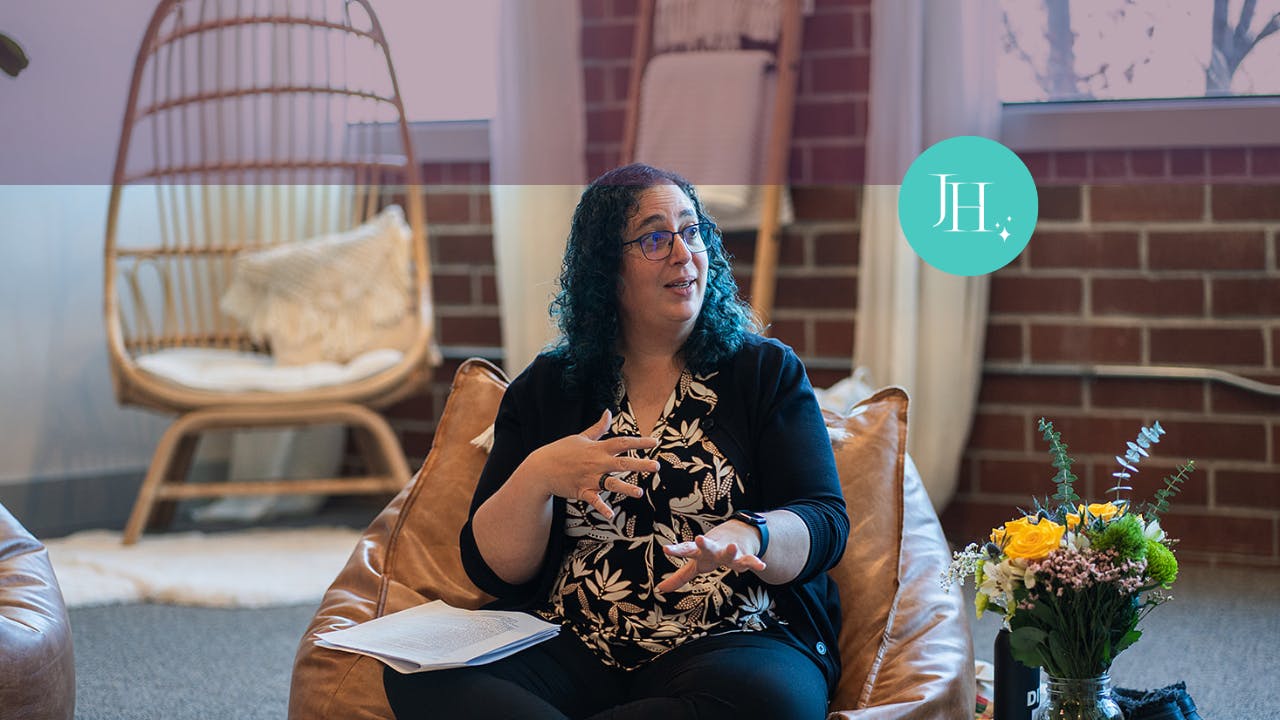 Jossie Hianes, leadership coach for women in tech, is sitting on a chair, talking with a group of women about leadership. She is gesturing with her hands as she speaks.